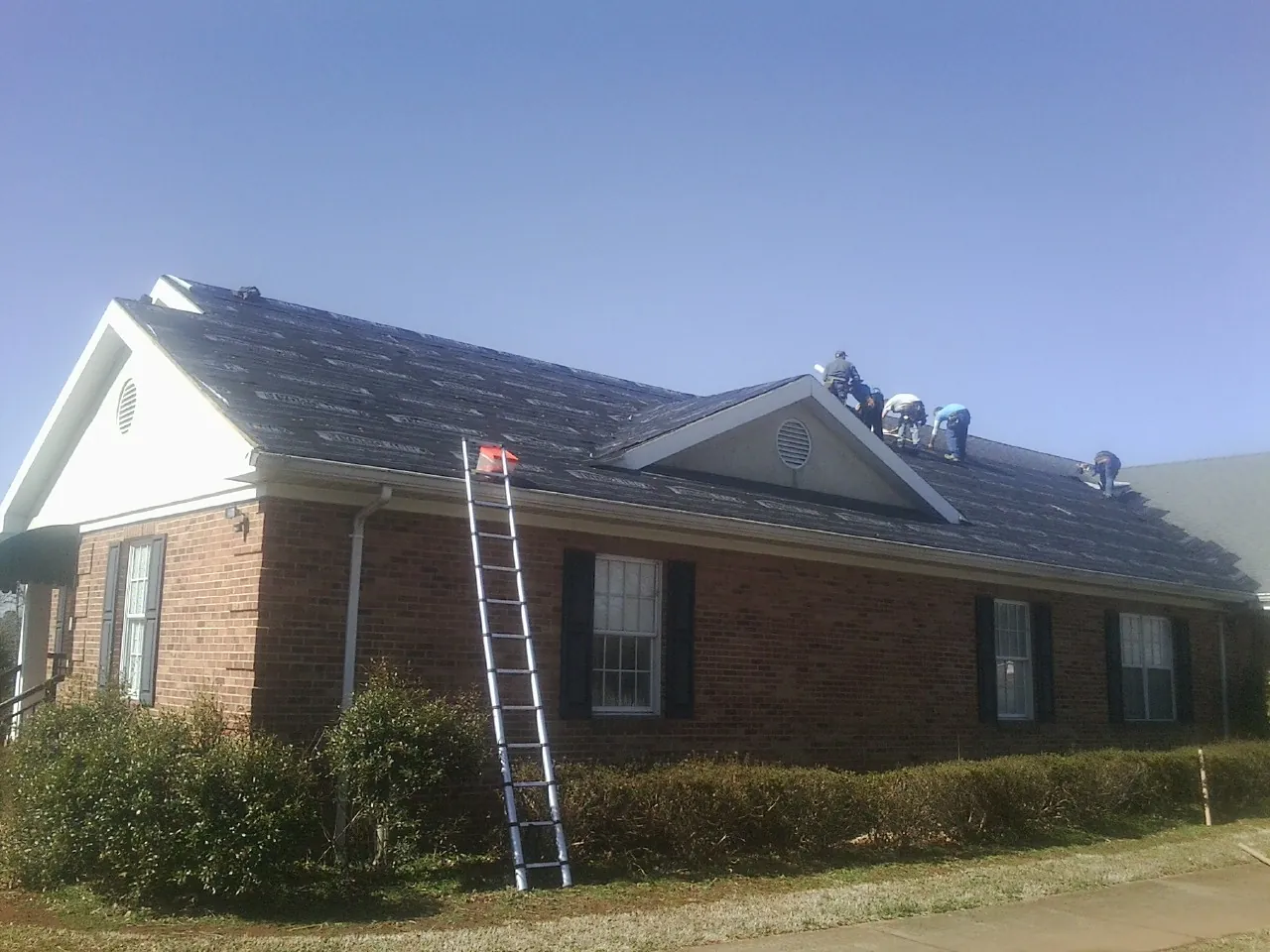 Crew tearing shingles off a brick ranch roof with a ladder set — Metal Roof Repair work by our crew in Tellico Plains