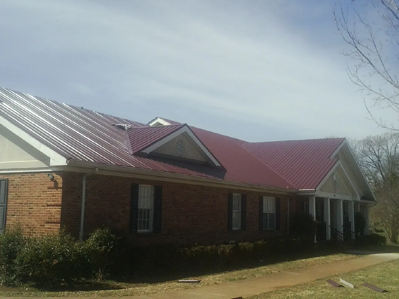 Red metal roof with gabled entries on a long brick building, from a Hail Damage Roof Repair job in Tellico Plains