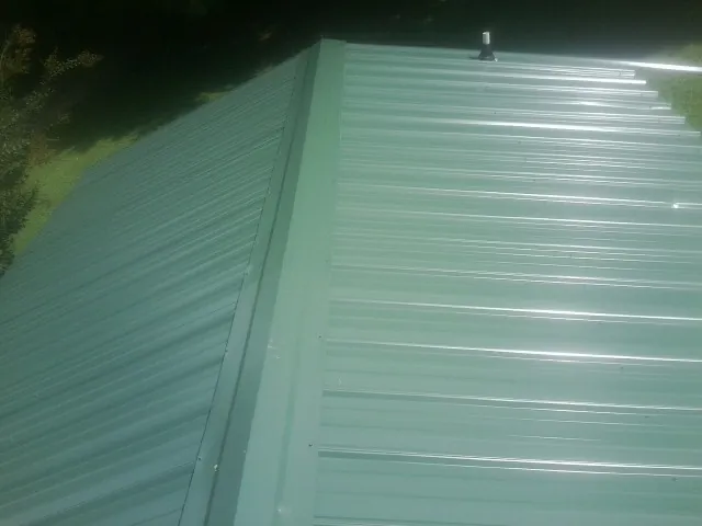 New green metal panels meeting at the ridge of a roof — Flat Roof Repair work by our crew in Tellico Plains