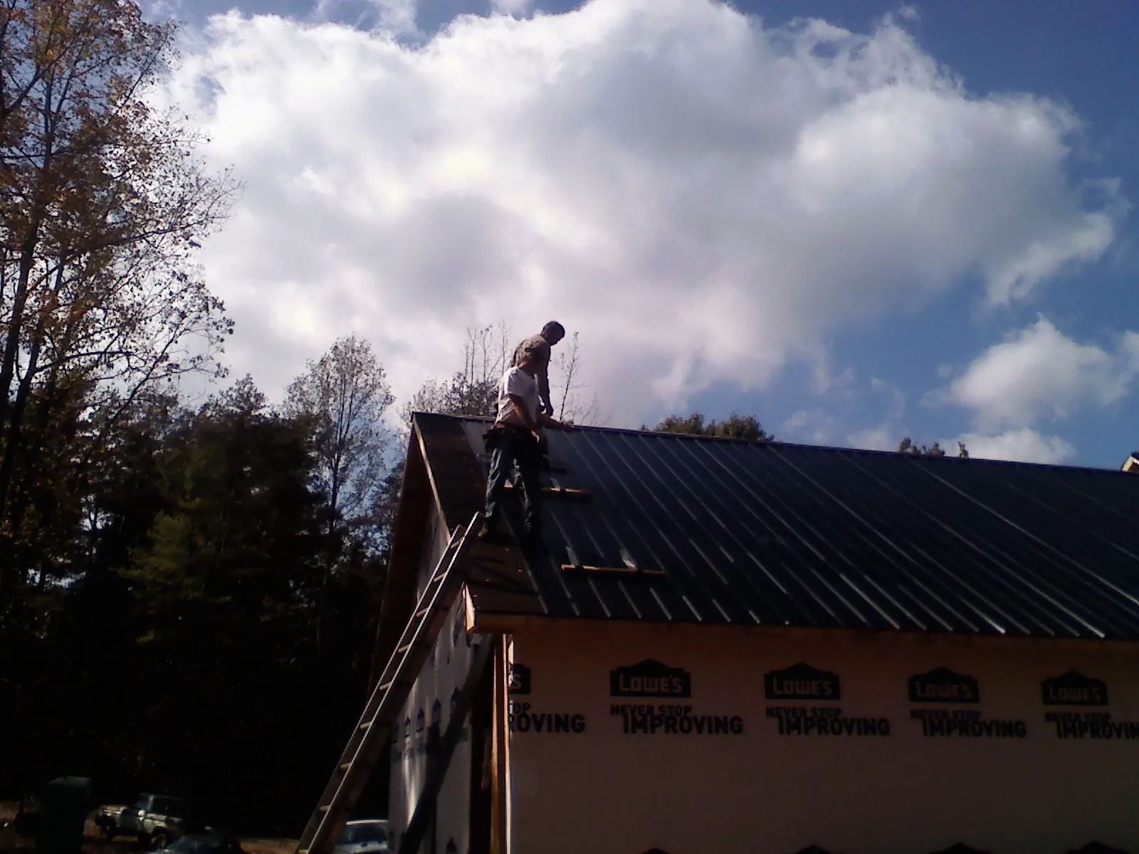 Roofer fastening dark metal panels high against a cloudy sky, from a Roof Inspection job in Tellico Plains
