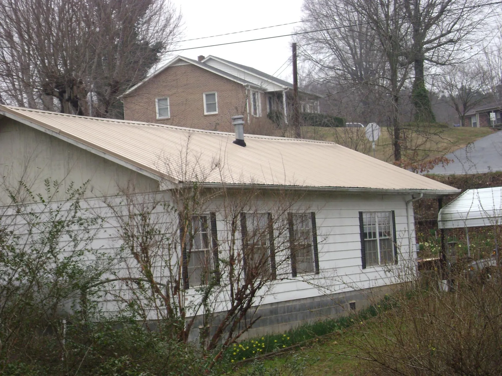 Tan metal roof on a white sided house set into a hillside — Commercial Roofing by Roofing Brothers in Tellico Plains