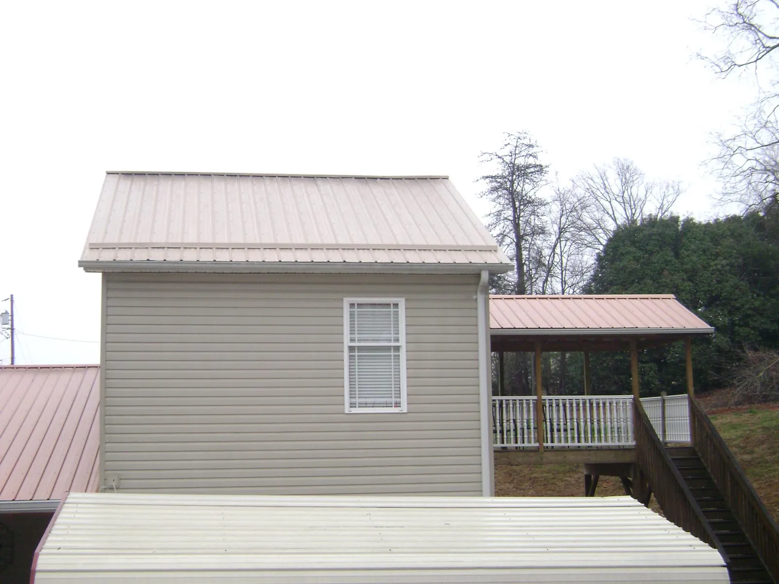 Tan metal roofs on a two story addition and attached porch, from a Roof Replacement job in Tellico Plains